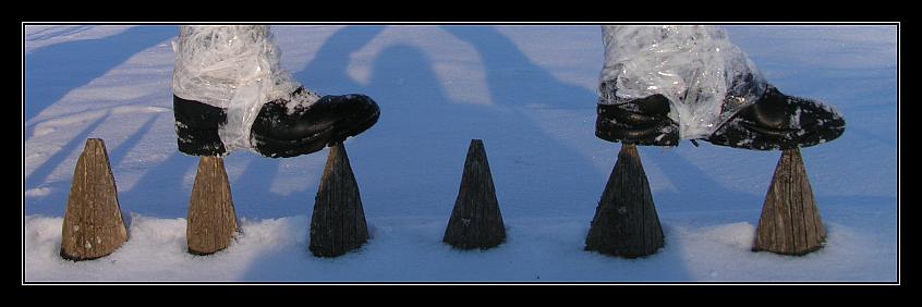 Zaunspitzen ragen aus dem Schnee und darauf sieht man zwei Schuhe
