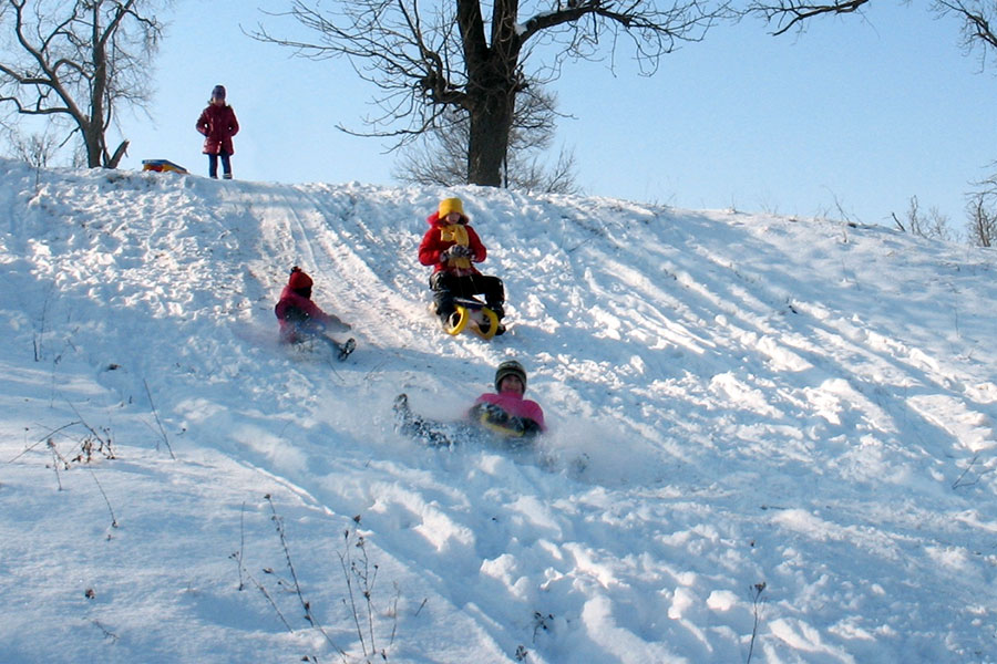 Kinder mit Po-Rutscher und Schlitten rutschen einen Berg hinunter