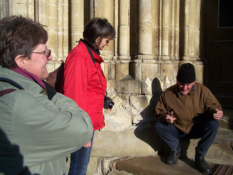 Mann hockt vor neben einer Kircheneingangssäule und erklärt Besuchern etwas