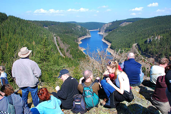 Foto von Menschen auf einem Berg vor einem Stausee umgeben von Wald