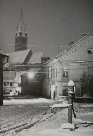 verschneite Straße mit Wasserpumpe im vordergrund und Kirche im Hintergrund