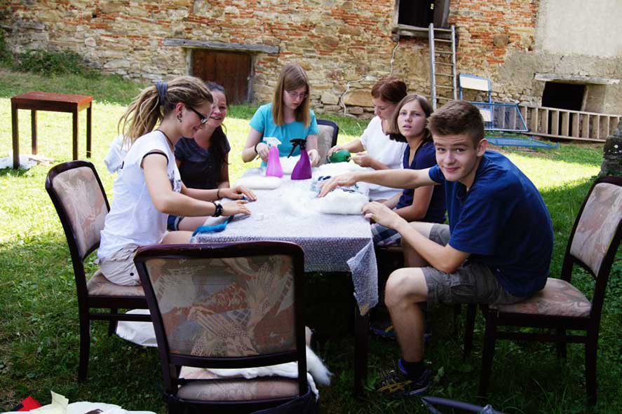Jugendlich sitzen bastelnd an einem Tisch im Garten