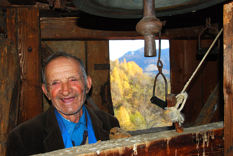 Mann steht lachend unter einer Glocke auf dem Kirchturm