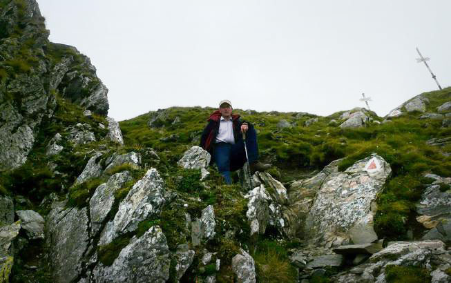 Christian sitzt mit Wanderstock zwischen Felsblöcken im Gras