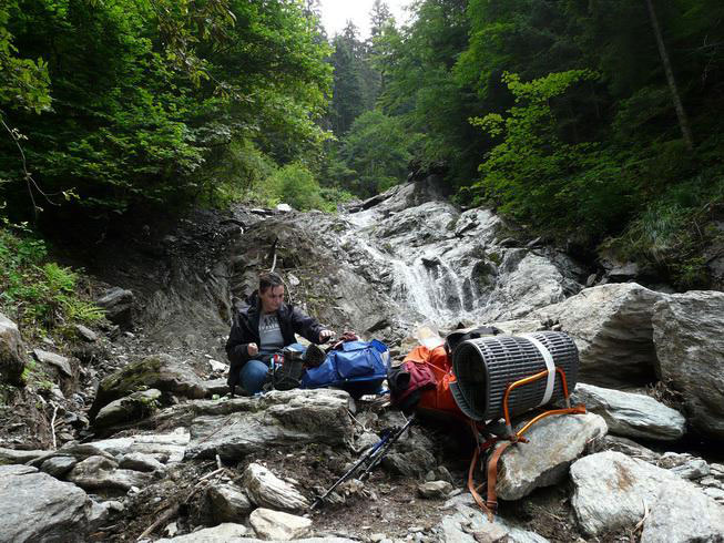 Rucksack lehnt an einem Felsen vor einem kleinen Wasserfall