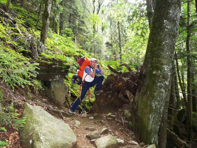 Christian lehnt ich mit einem Rucksack auf den Rücken an einen Holzstapel