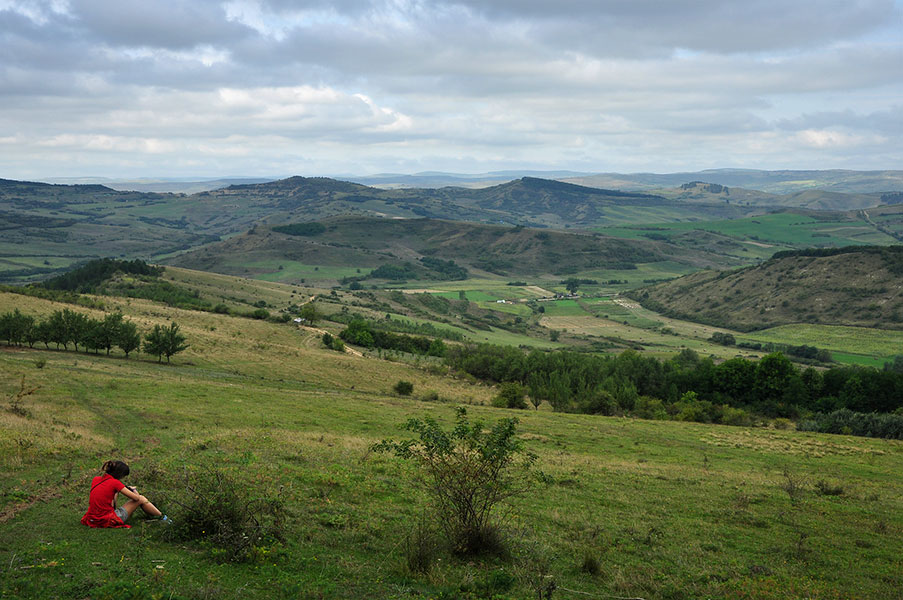 Mädchen sitzt auf der Wiese und schaut in die hügelige Heidelandschaft