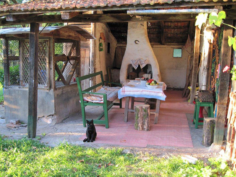 überdachter Gartentisch mit Bank vor einem Grill und daneben ein Brunnen