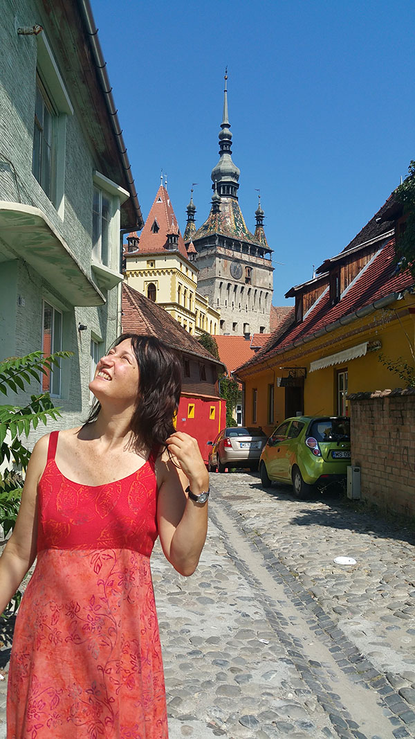 Frau steht in einer Gasse mit alten bunten Häusern mit einem Turm im Hintergrund