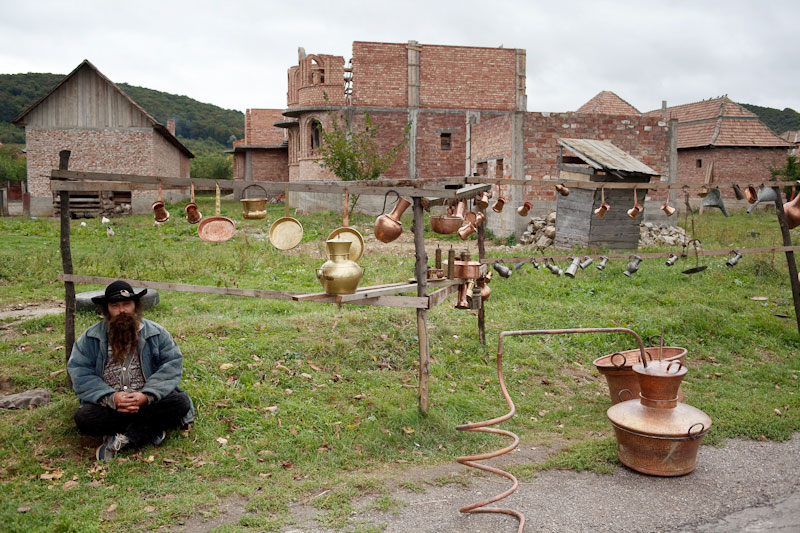Mann sitzt vorf einem Verkaufsstand von Kupferkesseln