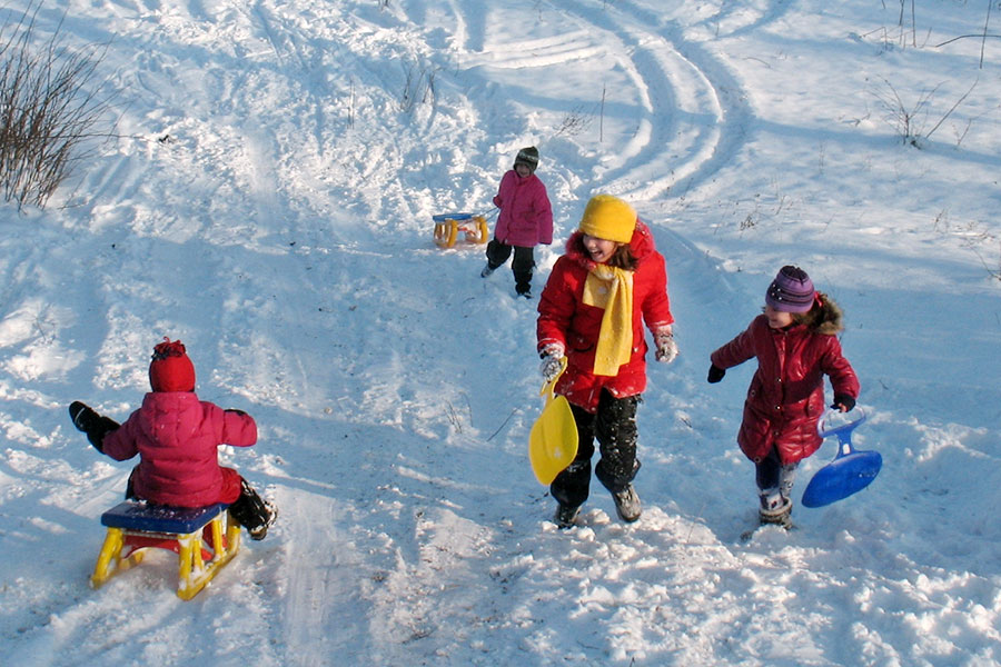 Kinder mit Po-Rutscher und Schlitten gehen einen Berg hinauf