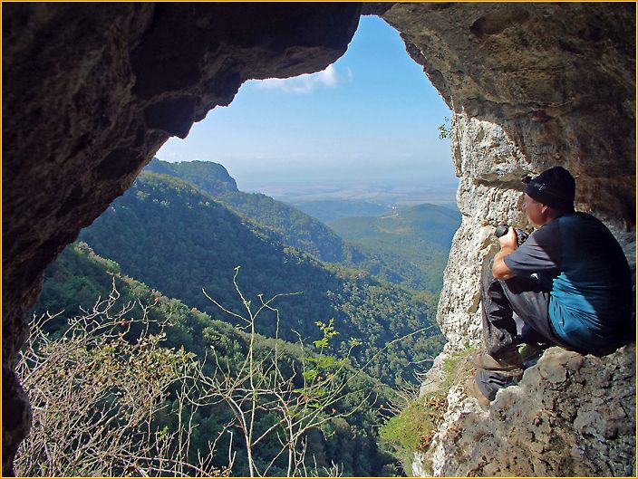 Hans sitzt in einem Felsfenster und schaut in die bewaldete Berglandschaft