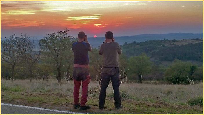 Hans und Willi stehen am Straßenrand und fotografieren einen Sonnenuntergang