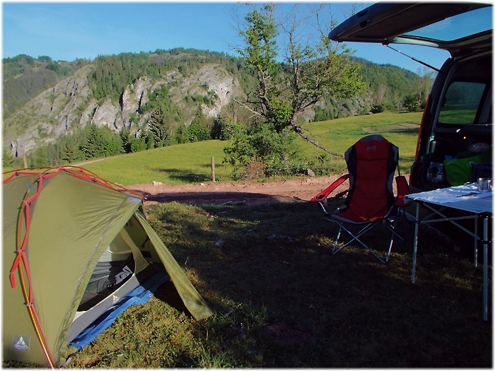 Zelt und Auto und ein Campingtisch stehen auf einer Wiese vor einem Felsmassiv