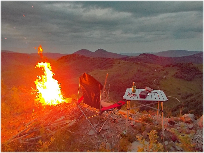 Lagerfeuer neben Campingtisch und Weitsicht auf Berglandschaft