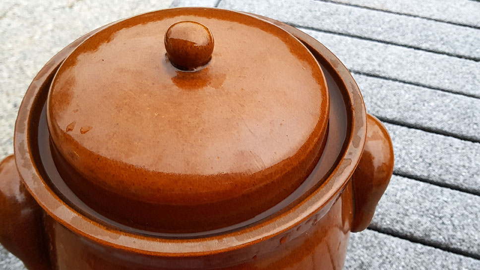 Tonkrug mit Wasser abgedichtetem Deckel auf dem verschneiten Tisch stehend.