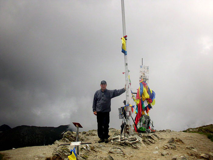 Stefan steht auf dem Gipfel und hält sich an einem MAst fest