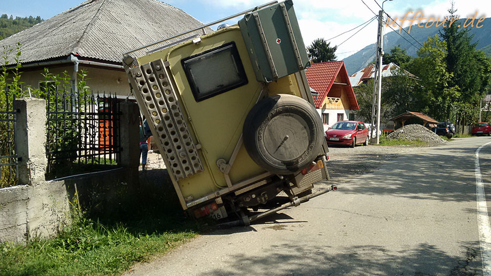 Wohnmobil-LKW ist mit dem linken Hinterrad im Loch verschwunden und lehnt links an einem Betonpfeiler