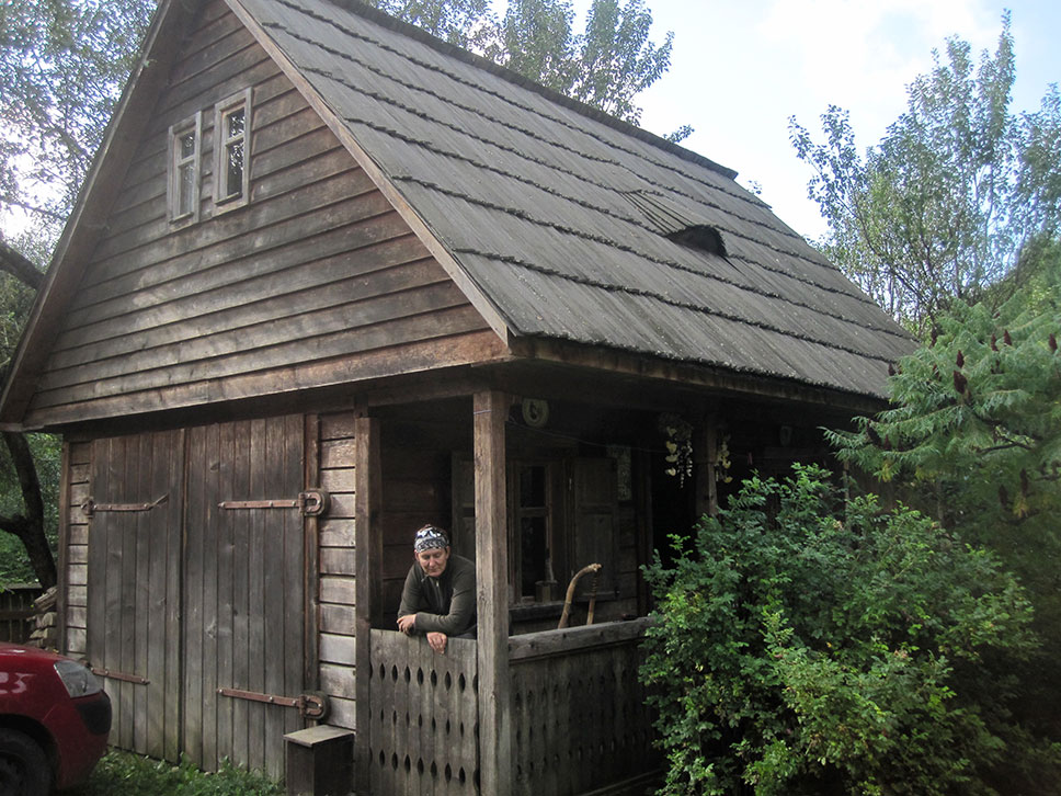 Winnie steht am Tor des Vorbaus eines alten Holzhauses