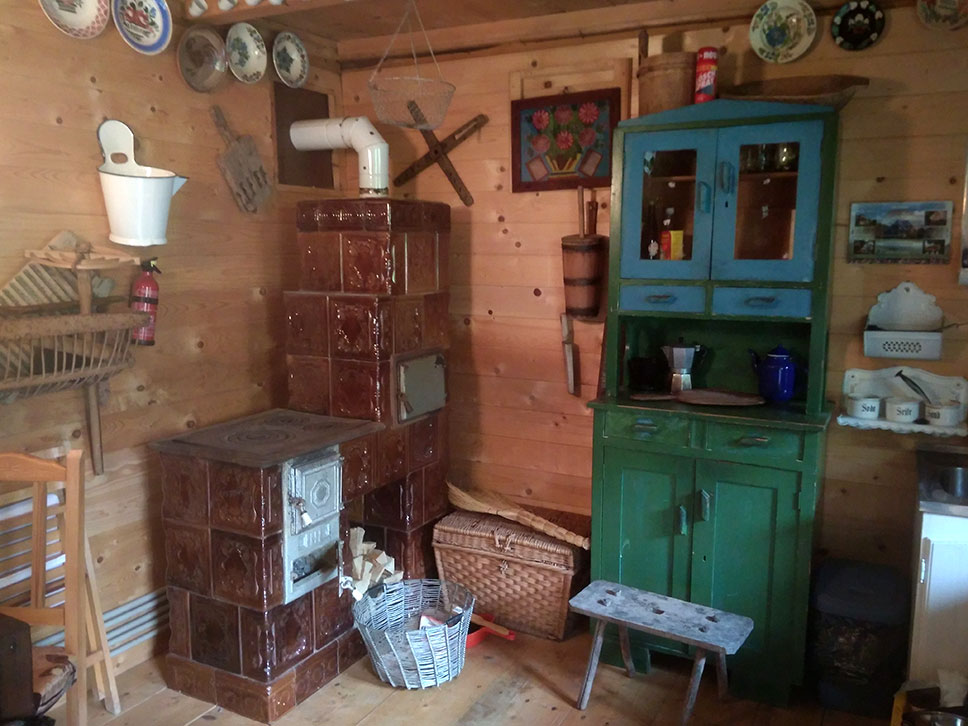 Innenraum mit altem Kachelofen mit kombinierter Kochstelle nebem einem Holzschrank vor einer Holzwand