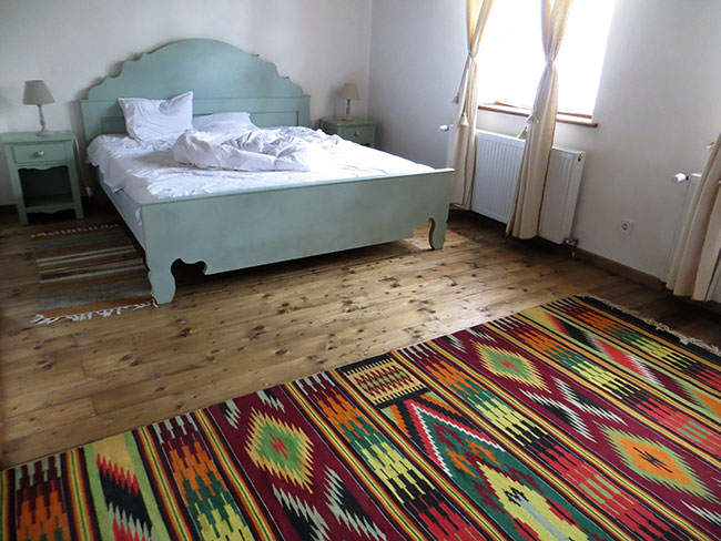 Gästezimmer mit selbstgebautem blauen Holzbett und buntem handgewebtem Teppich davor