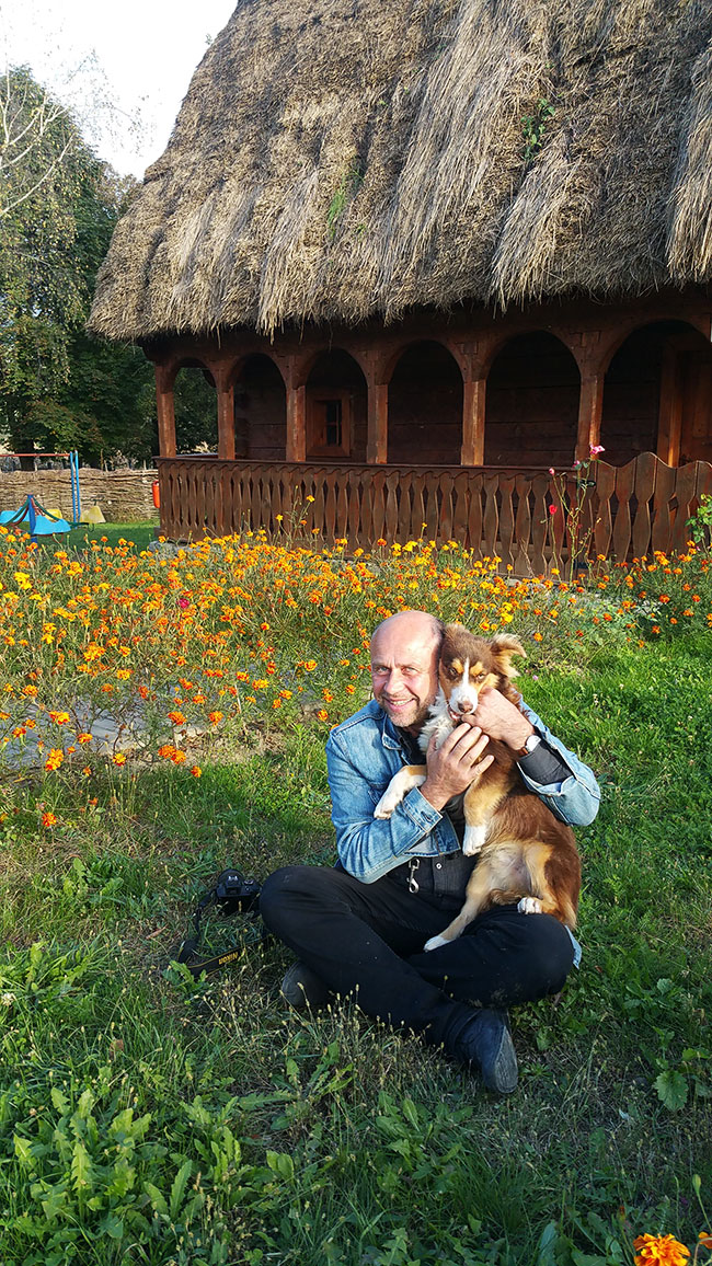 Mann mit Hund vor einem Motzenhaus kniend in die Kamera schauend