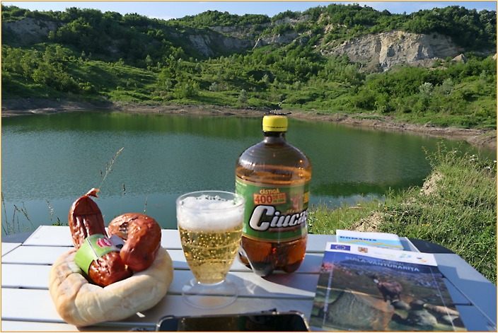 Campingtisch mit Bier, Wurst, Brot und Zeitung an einem See