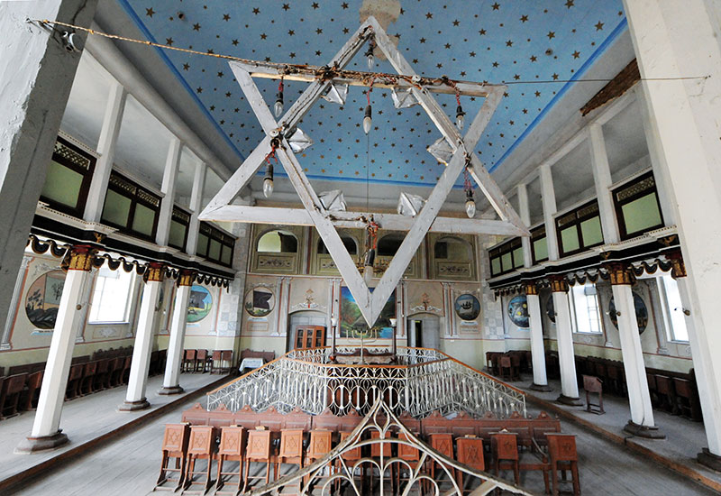 Innenraum der Synagoge mit blauer Deckenbemalung und mit Metallgeländer eingezäumten Toraschrein in der Mitte