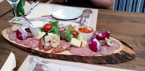 Holzpaltte auf dem Tisch stehend mit verschiedenen Käse-, Wurst- und Fleischsorten garniert, dazu Zwiebeln, Tomaten, eine helln und eine rote Soße