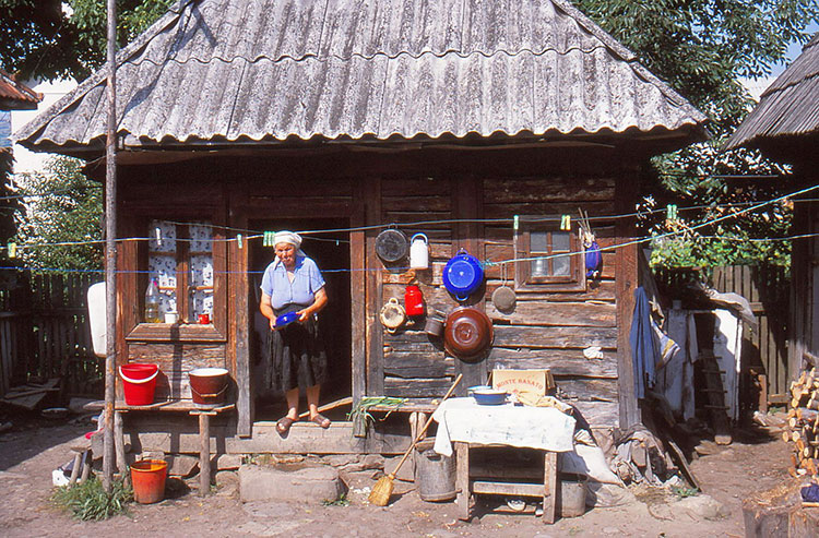 Foto von altem Holzhaus mit Töpfen and der Hauswand und einer Frau in der Tür stehend