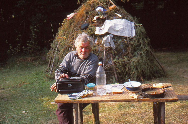 Mann sitzt an einem Tisch mit Radio, Teller und einer Plasteflasche