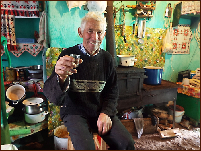 Bauer mit Schnapsglas in der Hand in der Küche sitzend