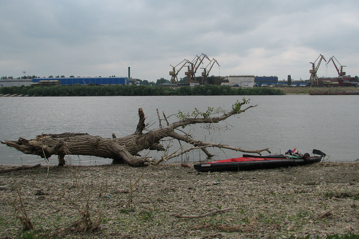Kajak am Flußufer und Industrieanlage am anderen Donauufer mit mehreren riesigen Kränen