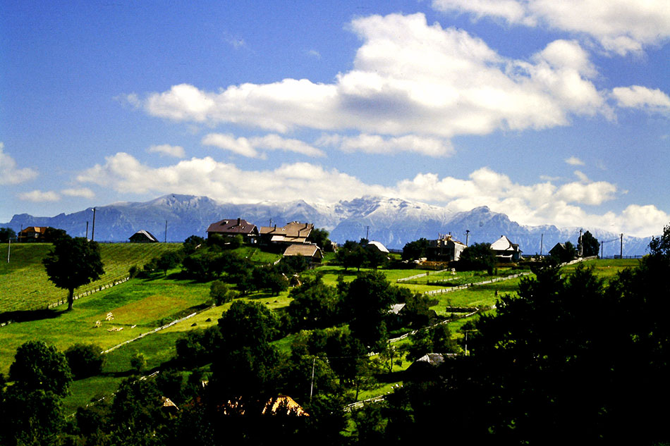 Hügelkette mit Dorf vor Bergmassiv