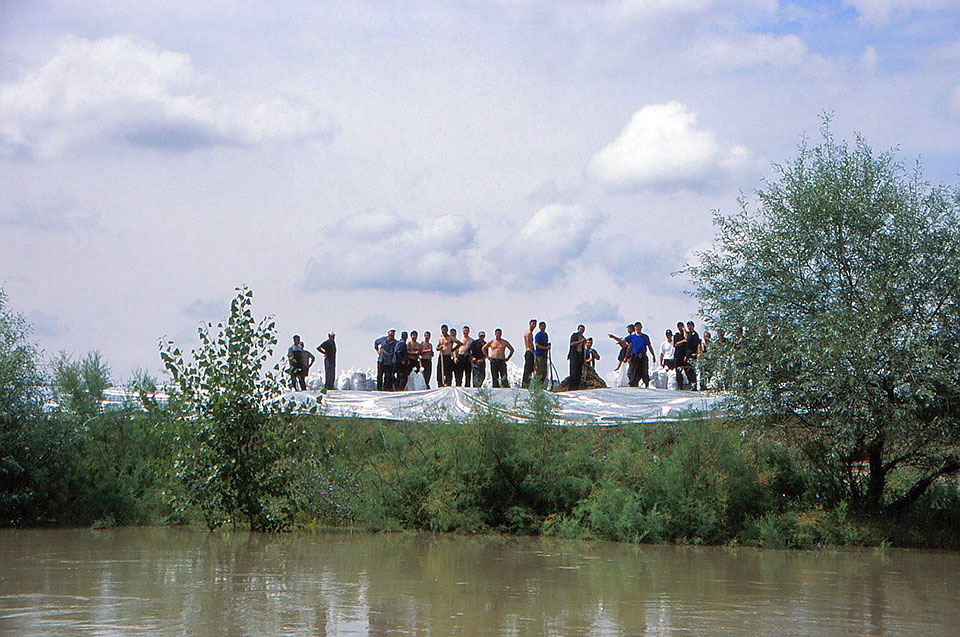 Männer stehen am Flussrand und bauen Hochwasserbarrikaden