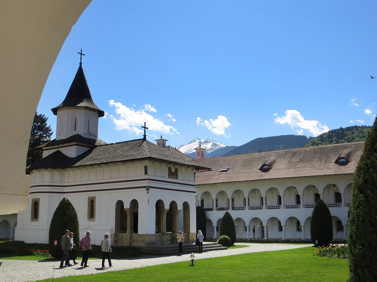 Klosteranlage mit grüner Wiese und verschneiter Gebirgsspitze im Hintergrund