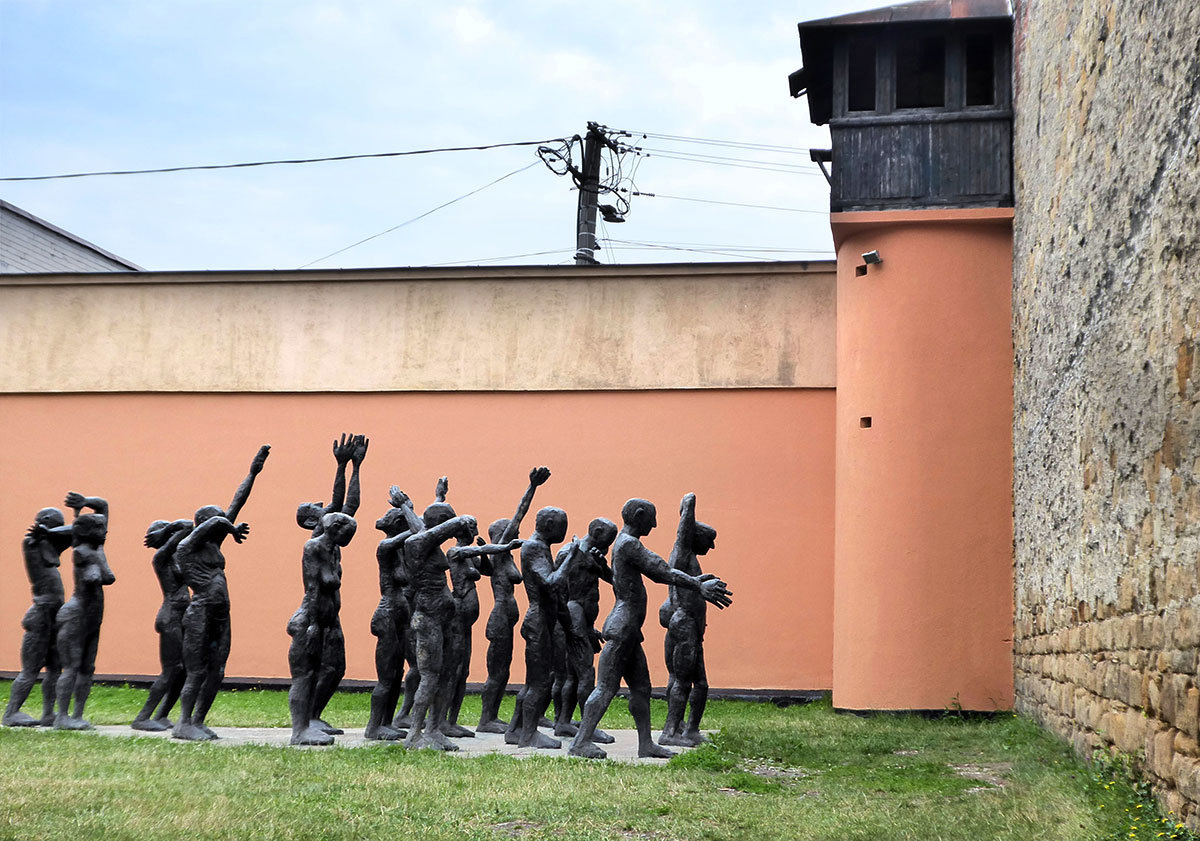 Bronzefiguren mit teilweise erhobenen Armen vor einer Wand im hof stehend
