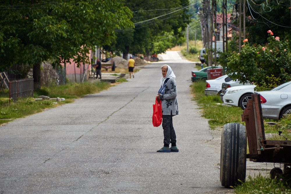 Frau steht mit roter Einkaufstasche auf einer Dorfstraße
