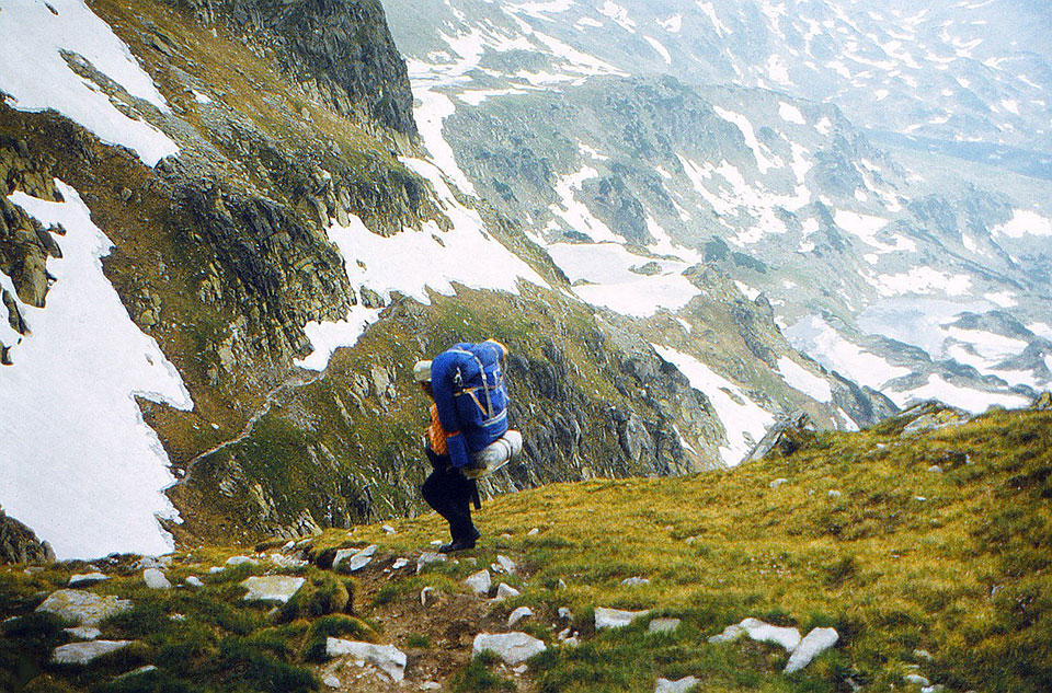 Berge mit Schneefeldern und Wanderer mit großem Rucksack