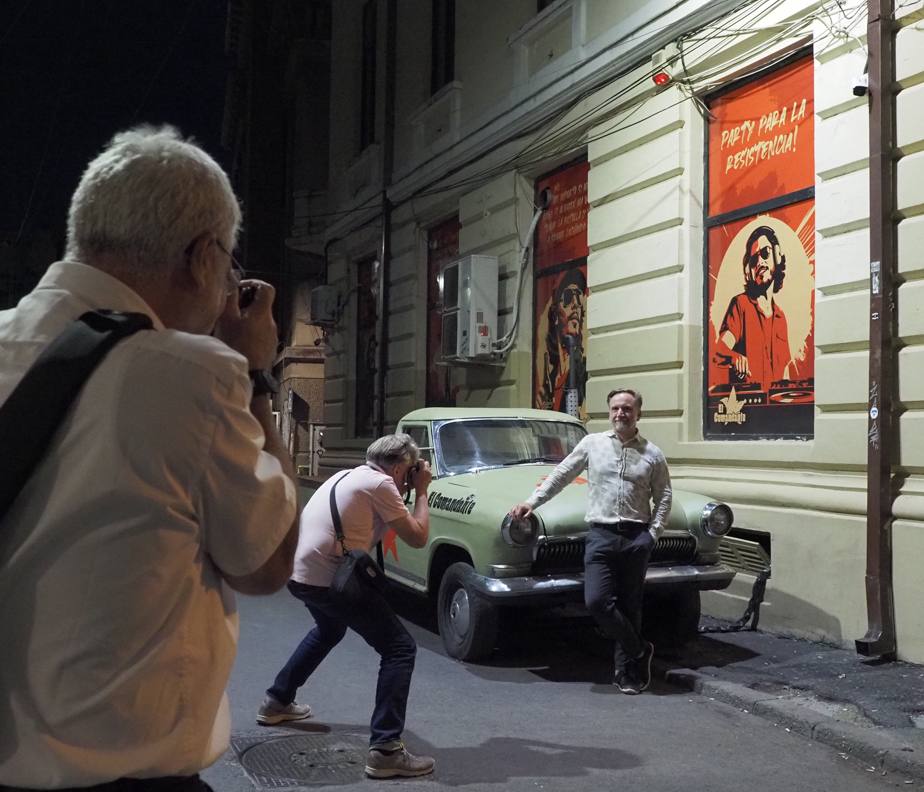 Männer fotografieren Mann vor einem Auto