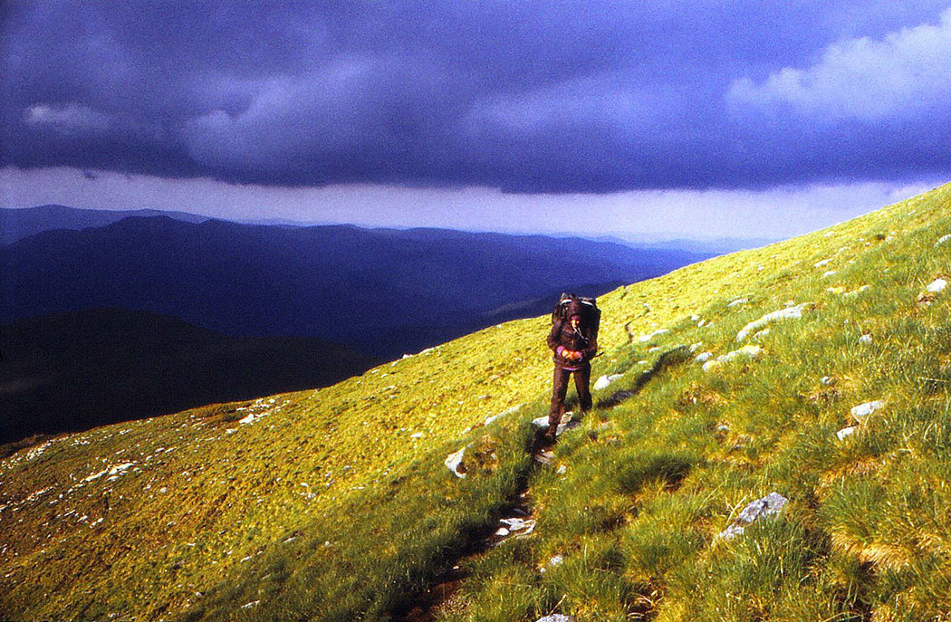 Frau wandert in Berglandschaft mit dunklen Wolken im Hintergrund