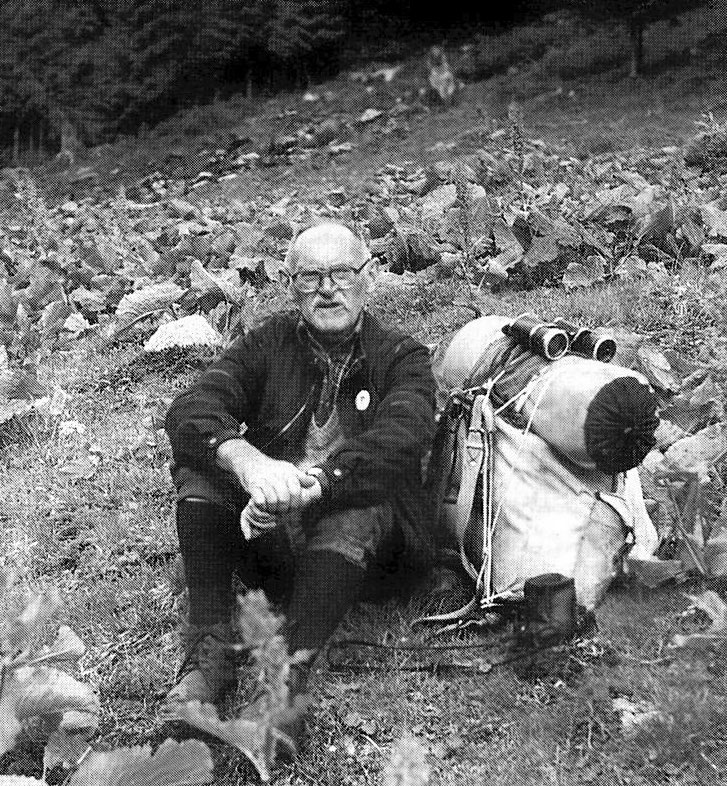 Mann sitzt neben seinem Rucksack auf einer Wiese