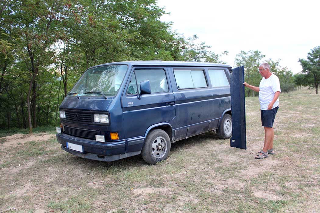 Mann mit abgefallenem Blech neben dem Auto