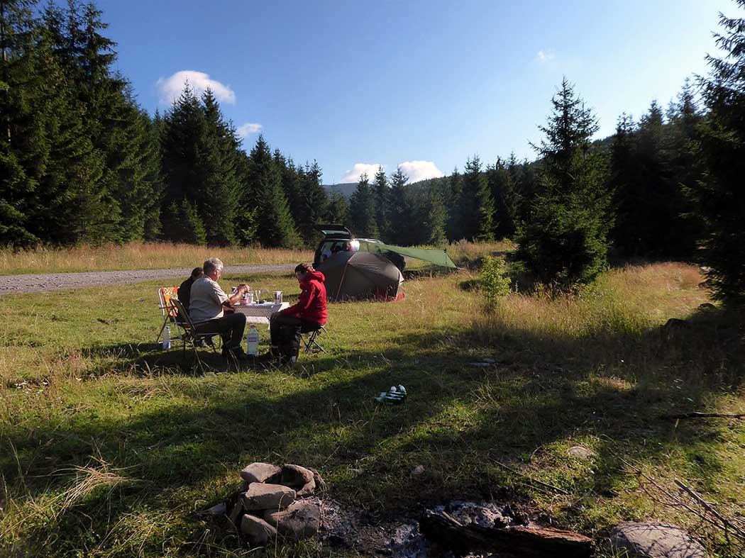 Menschen sitzt am Essenstisch auf einer Wiese neben einem Zelt